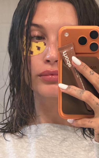 Hailey Bieber wears an opaque white manicure. She also wears under eye patches and has wet hair.